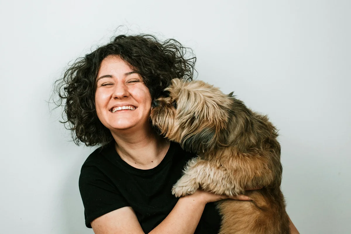 An owner smiling as her dog nuzzles her cheek